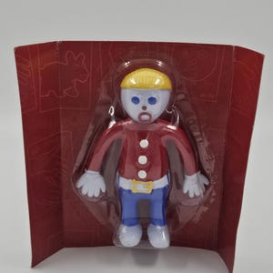 May include: A plastic toy figure of a person in a red jacket, blue trousers, and a yellow hat, packaged in a red cardboard container. The figure has white gloves and shoes, and a dummy. The packaging has a cartoon drawing of a rabbit.