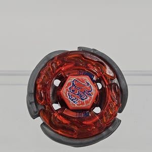 Peut inclure: Un toupie rouge et grise. La toupie a un anneau ext&eacute;rieur rouge transparent et un anneau ext&eacute;rieur gris. Le centre pr&eacute;sente un graphisme rouge et bleu. Le jouet est con&ccedil;u pour tourner et combattre.