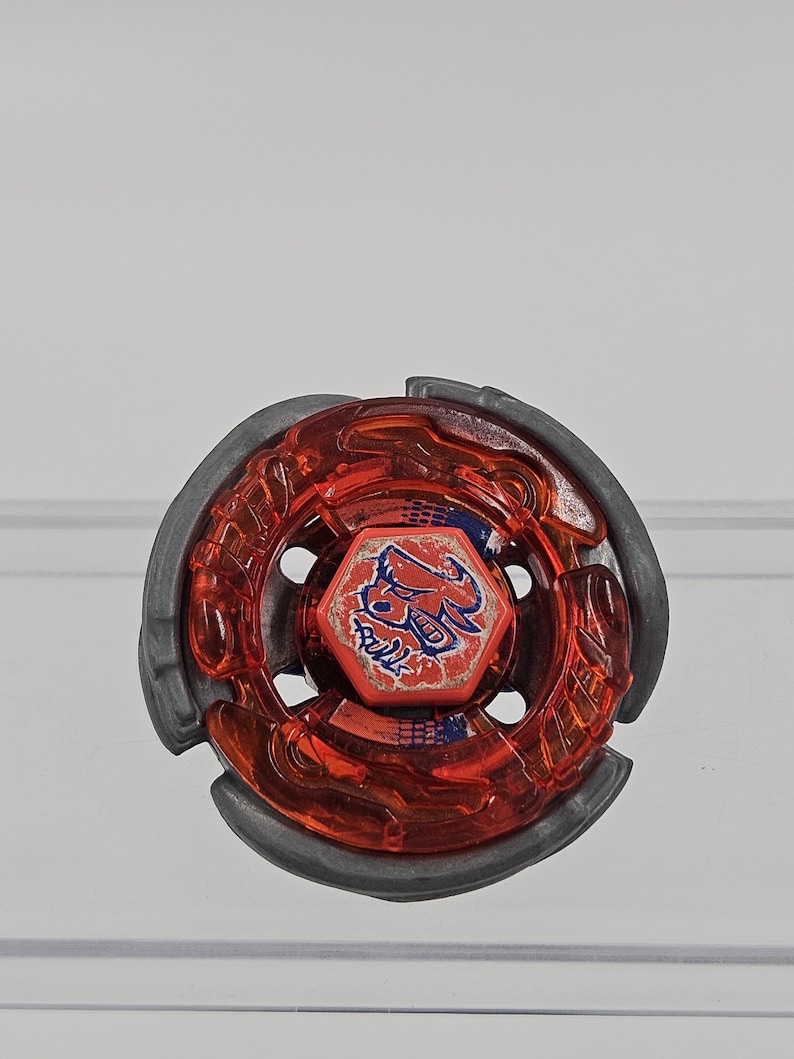 Peut inclure: Un toupie rouge et grise. La toupie a un anneau ext&eacute;rieur rouge transparent et un anneau ext&eacute;rieur gris. Le centre pr&eacute;sente un graphisme rouge et bleu. Le jouet est con&ccedil;u pour tourner et combattre.