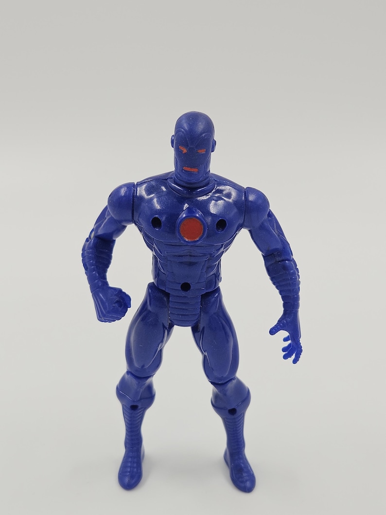 May include: A blue action figure of a humanoid robot with a red circular chest emblem and red eyes. The figure is standing with its arms slightly bent and its hands open. The figure has a smooth, glossy finish.