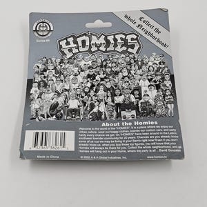 May include: A grey cardboard backing for a Homies collectible toy figure, featuring a crowd of cartoon characters. The text reads "HOMIES" in large letters, with "Collect the whole neighbourhood!" above. Series #4 is also visible.