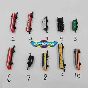 May include: A collection of ten Micro Machines toy train cars in various colors, including red, black, white, green, yellow, and orange. The cars are arranged on a white surface with the Micro Machines logo in the center.