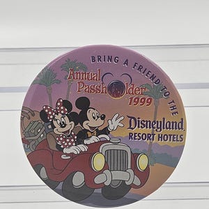Op de afbeelding: Een ronde knop in paars en oranje met Mickey en Minnie Mouse die een rode auto rijden. De knop heeft de tekst "Bring a Friend to the Disneyland Resort Hotels" en "Annual Passholder 1999".
