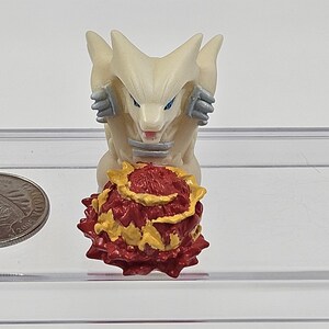 May include: White and grey figurine of a wolf-like creature with blue eyes, sitting on a red and yellow spiky ball.