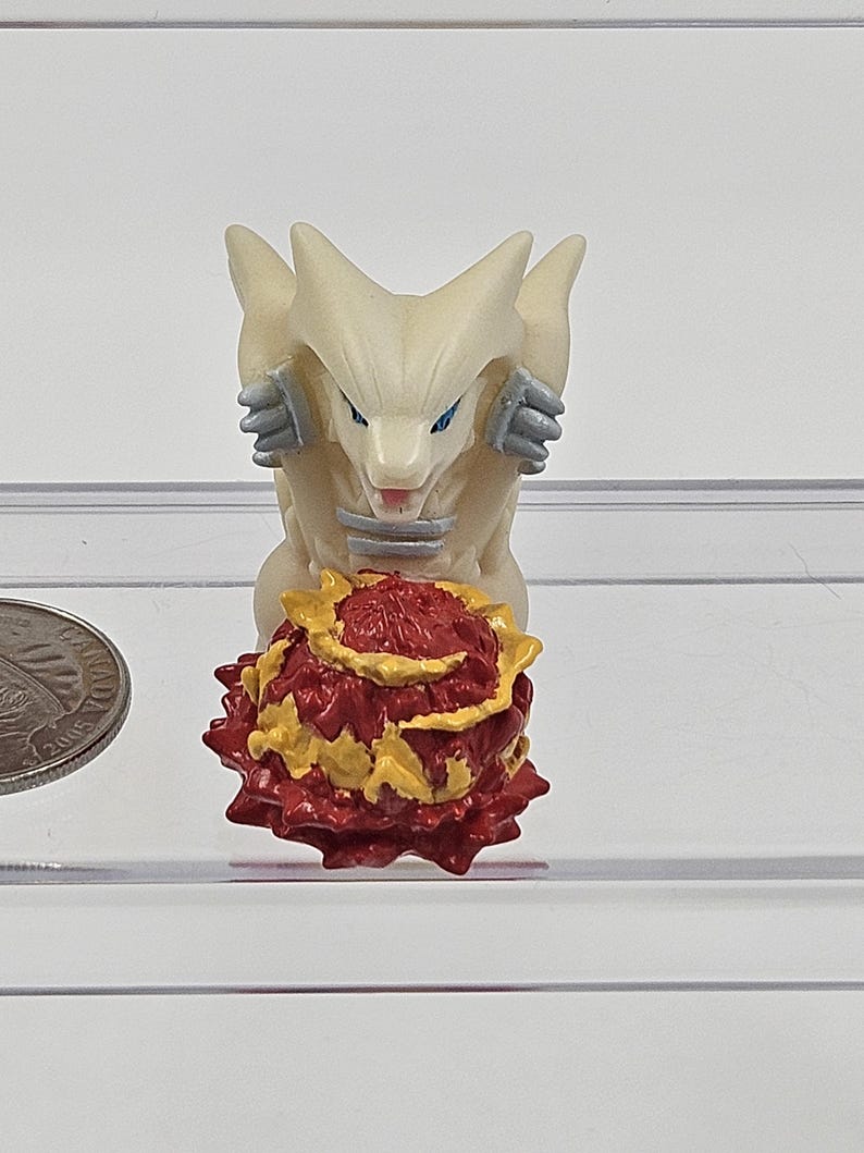 May include: White and grey figurine of a wolf-like creature with blue eyes, sitting on a red and yellow spiky ball.