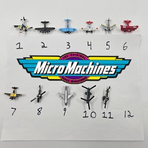 Puede incluir: Una colección de doce aviones y helicópteros de juguete Micro Machines. Los juguetes son de varios colores, incluyendo negro, azul, rojo y plateado. El logotipo de Micro Machines es visible en el papel.