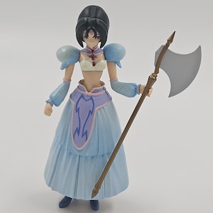 May include: A detailed figurine of a female character in a light blue dress with puffy sleeves and a purple waist. She holds a staff with a silver axe head. The figure has black hair and is posed against a plain background.