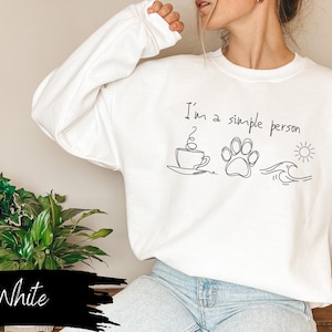 May include: White sweatshirt with the text "I'm a simple person" and illustrations of a cup of coffee, a paw print, and a wave.