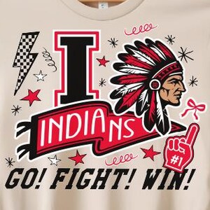 May include: Beige t-shirt with a graphic design featuring the word "INDIANS", a Native American profile, and the phrases "GO! FIGHT! WIN!" and "#1". The design includes stars, lightning bolts, and decorative elements.