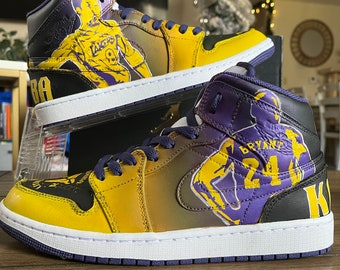 May include: A pair of yellow, purple, and black sneakers with a graphic of Kobe Bryant wearing a Los Angeles Lakers jersey. The sneakers have a white midsole and a purple outsole.