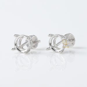 May include: A pair of silver earring settings with a round bezel for holding a gemstone. The settings have a post and butterfly backing.
