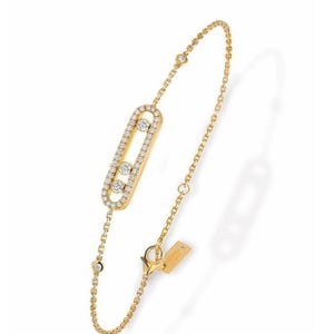 May include: A gold bracelet with a central oval, set with small diamonds. The oval is surrounded by a fine chain with diamond accents. A small tag is attached near the clasp. The bracelet is a piece of jewellery.