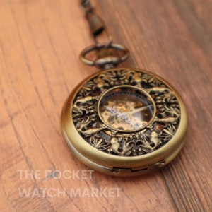 May include: A gold pocket watch with an intricate design featuring a detailed clock face and a chain attached to the top.
