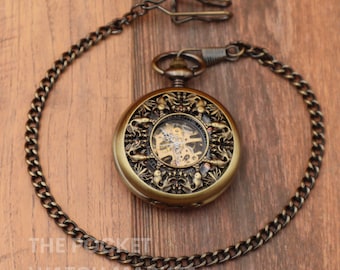 May include: A gold-toned pocket watch with a skeletonized movement and intricate floral design. The watch is attached to a chain.