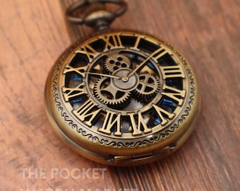 May include: A gold-toned pocket watch with a skeletonized face, revealing the inner workings of the clock. The watch has Roman numeral hour markers and blue accents.