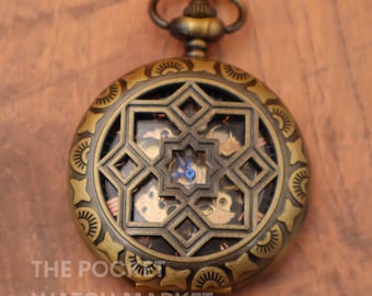 May include: A gold-toned pocket watch with an intricate, open-faced design. The watch face features a geometric pattern with a visible clock mechanism.