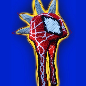 Puede incluir: Un gorro de crochet rojo y blanco con un diseño de Spiderman. El gorro tiene una parte superior puntiaguda y piernas largas y delgadas.
