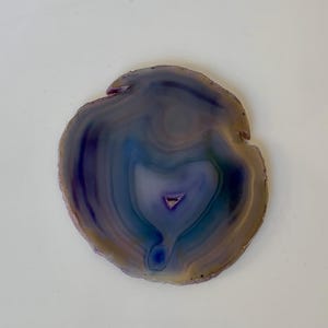 May include: A round agate coaster with a purple, blue, and white swirl pattern. The coaster is made of natural stone and has a smooth, polished surface.
