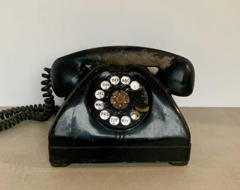 May include: A black rotary dial phone with a white dial face and black rotary dial. The dial face has the letters ABC, DEF, GHI, JKL, MNO, PRS, TUV, WXY.