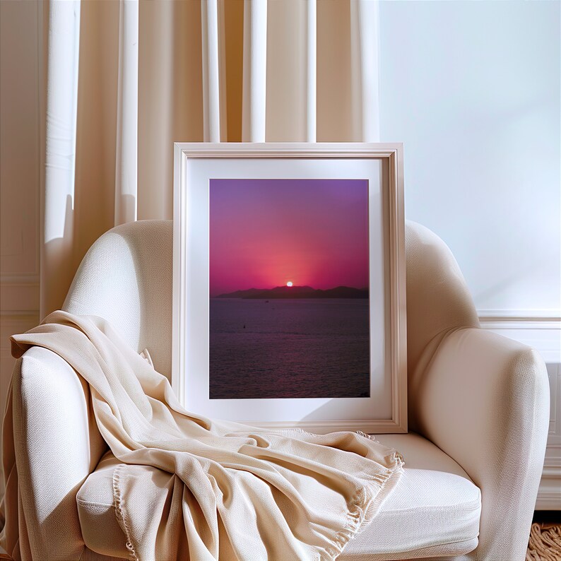 Radiant purple sunset photography framed and placed on a cozy armchair with light beige modern background decor. The print's pink and purples hues beauty are highlighted in this simple yet stylish decor