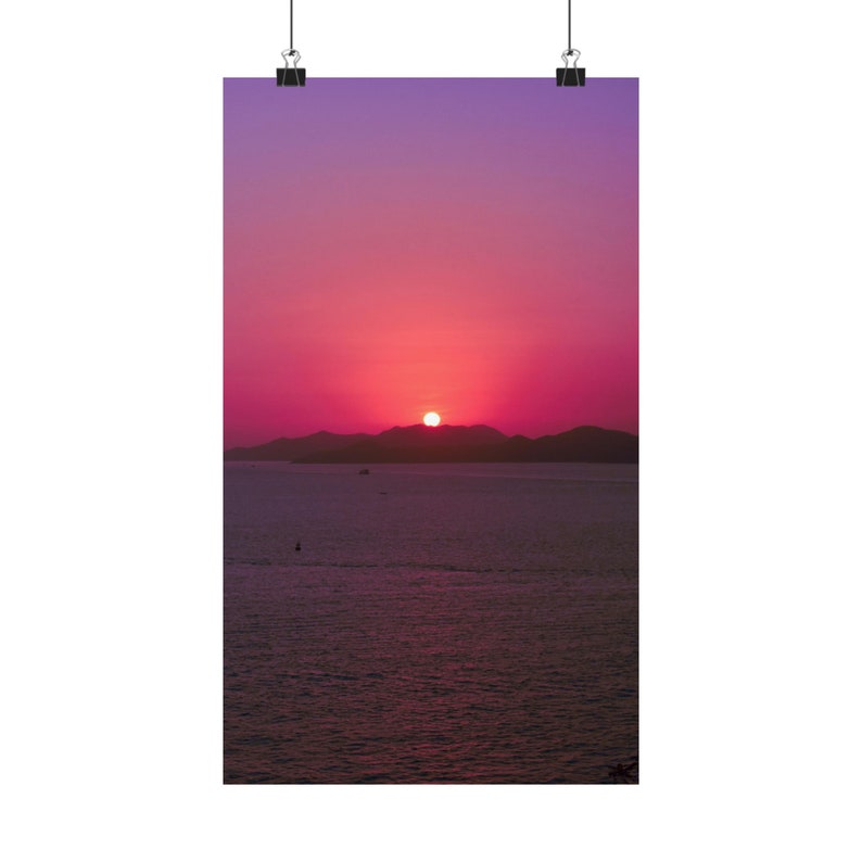 A radiant sun is setting on dark hills and the ocean horizon. The sun has stunning colors and gives the sky beautiful pink and purple hues. The sea is calm and dark in contract with the colorful sky. A single boat crosses the calm sea
Size: 10" x17"