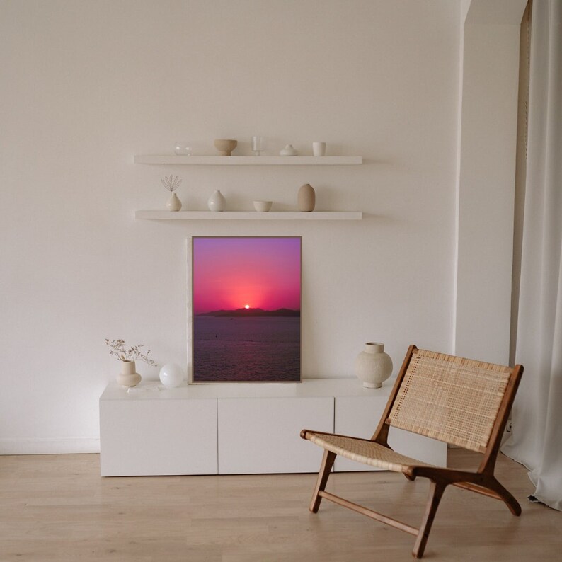 Stunning purple sunset on ocean poster in a minimalist boho living room, with white and light colors decor. The room has a serene and soothing ambiance