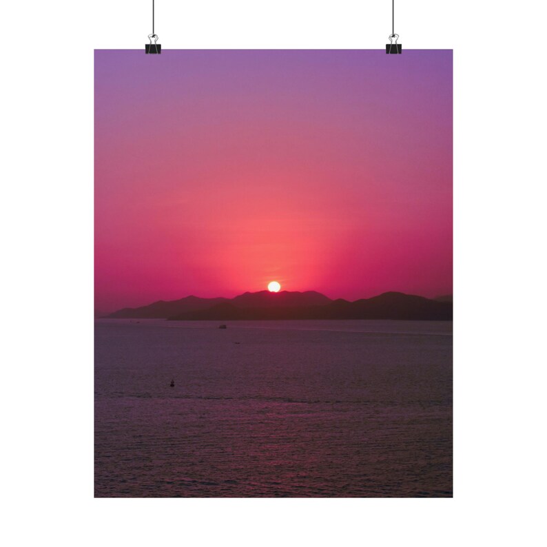 A radiant sun is setting on dark hills and the ocean horizon. The sun has stunning colors and gives the sky beautiful pink and purple hues. The sea is calm and dark in contract with the colorful sky. A single boat crosses the calm sea
Size: 16" x 20"