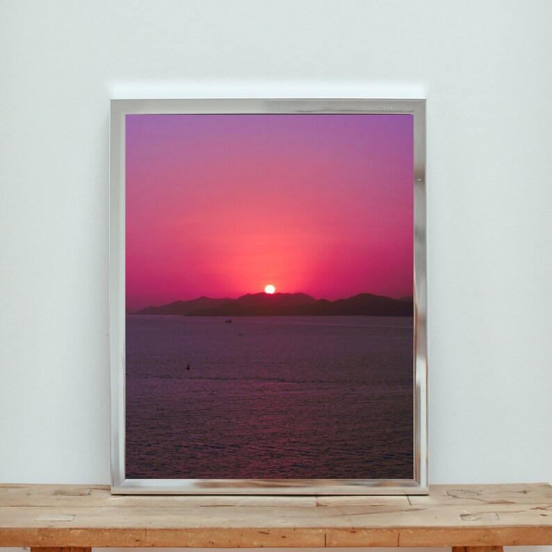 A purple sunset on ocean photography is framed in a silver frame and displayed on a wooden bench