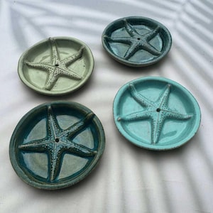 May include: Four ceramic dishes, each with a starfish design. The dishes are in shades of teal, turquoise, and seafoam green. The starfish are raised in the centre of each round dish, which has a slightly irregular edge.