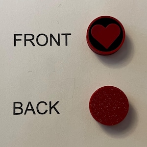 Puede incluir: Dos imanes rojos. Uno tiene un coraz&oacute;n rojo sobre un fondo negro. El otro im&aacute;n es rojo liso. Las palabras "FRONT" y "BACK" est&aacute;n impresas en la superficie blanca.