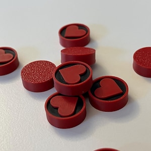 Puede incluir: Varios objetos circulares rojos con un dise&ntilde;o de coraz&oacute;n. Algunos tienen una superficie texturizada, otros son lisos. Los corazones est&aacute;n en relieve sobre un fondo negro. Estos podr&iacute;an ser elementos decorativos o funcionales.