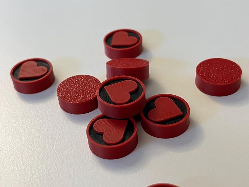 Puede incluir: Varios objetos circulares rojos con un dise&ntilde;o de coraz&oacute;n. Algunos tienen una superficie texturizada, otros son lisos. Los corazones est&aacute;n en relieve sobre un fondo negro. Estos podr&iacute;an ser elementos decorativos o funcionales.