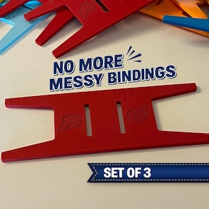 May include: Red, blue, yellow, and orange plastic binding tools. The red tool in the foreground has the text "NO MORE MESSY BINDINGS" and "SET OF 3". The tools have a unique shape with slots and circular designs.