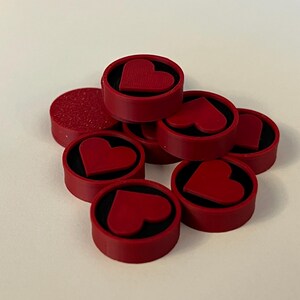 Puede incluir: Una colecci&oacute;n de objetos decorativos rojos en forma de coraz&oacute;n. Cada objeto tiene un exterior rojo con un interior negro y un dise&ntilde;o de coraz&oacute;n en relieve. Un objeto tiene una superficie texturizada. Los objetos est&aacute;n dispuestos sobre una superficie blanca.