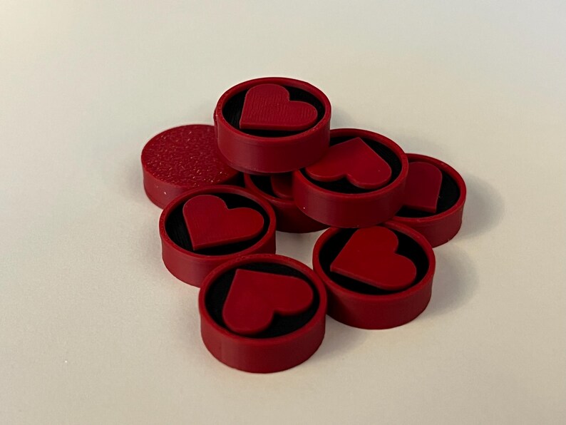 Puede incluir: Una colecci&oacute;n de objetos decorativos rojos en forma de coraz&oacute;n. Cada objeto tiene un exterior rojo con un interior negro y un dise&ntilde;o de coraz&oacute;n en relieve. Un objeto tiene una superficie texturizada. Los objetos est&aacute;n dispuestos sobre una superficie blanca.