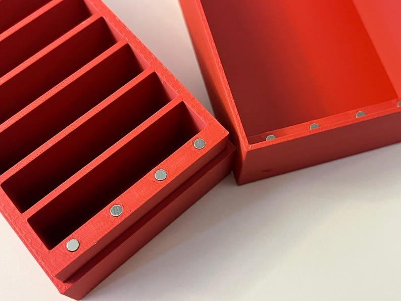 May include: A red wooden organizer with multiple vertical compartments, ideal for storing small items. The organizer is rectangular and has a matching lid. Small silver magnets are visible on the sides of the organizer and lid.