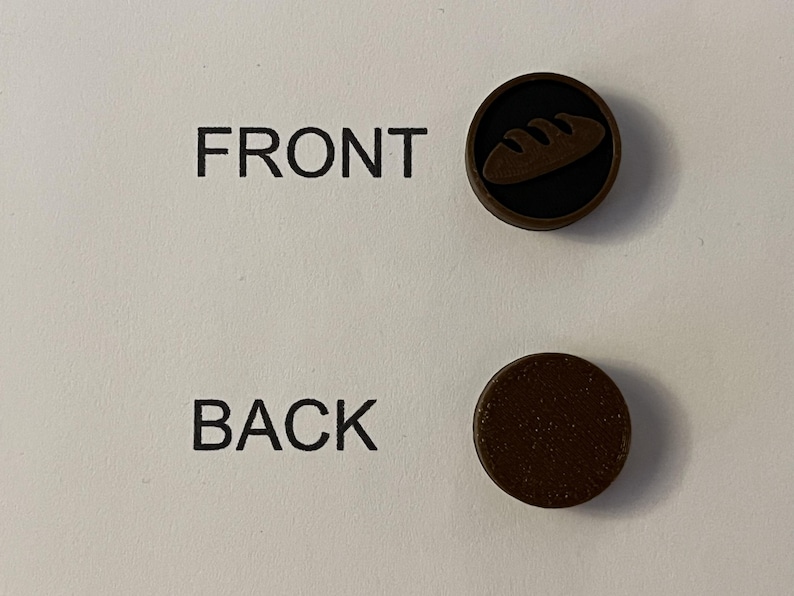 Puede incluir: Dos botones circulares marrones. Un bot&oacute;n tiene un fondo negro con un icono de pan. El otro bot&oacute;n es marr&oacute;n liso. Las palabras "FRONT" y "BACK" est&aacute;n impresas en el fondo blanco.