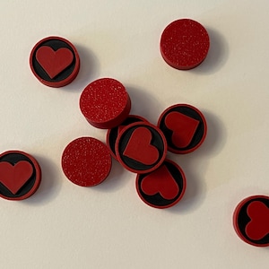 Puede incluir: Varios objetos circulares rojos con superficie texturizada sobre un fondo blanco. Algunos presentan un dise&ntilde;o de coraz&oacute;n rojo sobre una base negra. Podr&iacute;an ser elementos decorativos o componentes.