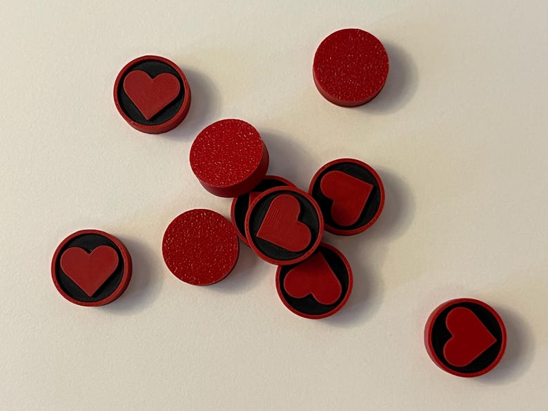 Puede incluir: Varios objetos circulares rojos con superficie texturizada sobre un fondo blanco. Algunos presentan un dise&ntilde;o de coraz&oacute;n rojo sobre una base negra. Podr&iacute;an ser elementos decorativos o componentes.