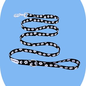 May include: Black and white daisy patterned dog lead with a silver metal clasp and D-ring. The lead is approximately 152 cm long. The brand name "pepper grey" is printed on the lead.