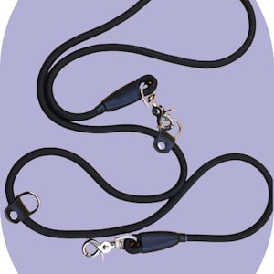 Puede incluir: Correa de perro de cuerda negra con dos clips metálicos y un mango de goma negro.