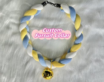 Puede incluir: Un collar de traje de piel trenzado en amarillo, blanco y azul claro con una campanilla dorada adjunta. El collar está hecho de tela suave y de felpa y está diseñado para usarse con un traje de piel.