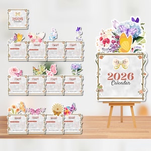 Op de afbeelding: Een verzameling 2026 kalenders met bloemen- en vlindermotieven. De kalenders worden gepresenteerd in een decoratieve opstelling, met verschillende formaten en stijlen, waaronder een grote ezelkalender. Het kleurenpalet omvat zachte pasteltinten en natuurlijke tinten.