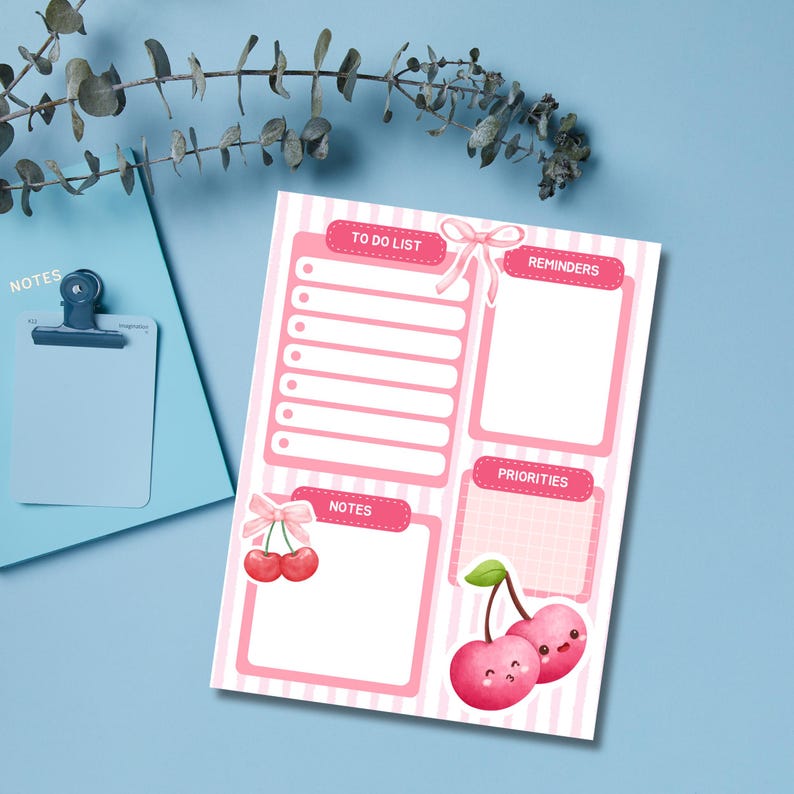May include: A pink and white striped to-do list notepad with sections for reminders, notes, and priorities. The notepad features a cherry illustration and the words "TO DO LIST", "REMINDERS", "NOTES", and "PRIORITIES". A blue clipboard is in the background.