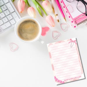 May include: A white desk scene with a cup of coffee, pink tulips, and stationery. A notepad with the text "Spread sunshine with a smile" is visible, along with heart-shaped paper clips and a keyboard. The scene is bright and airy.