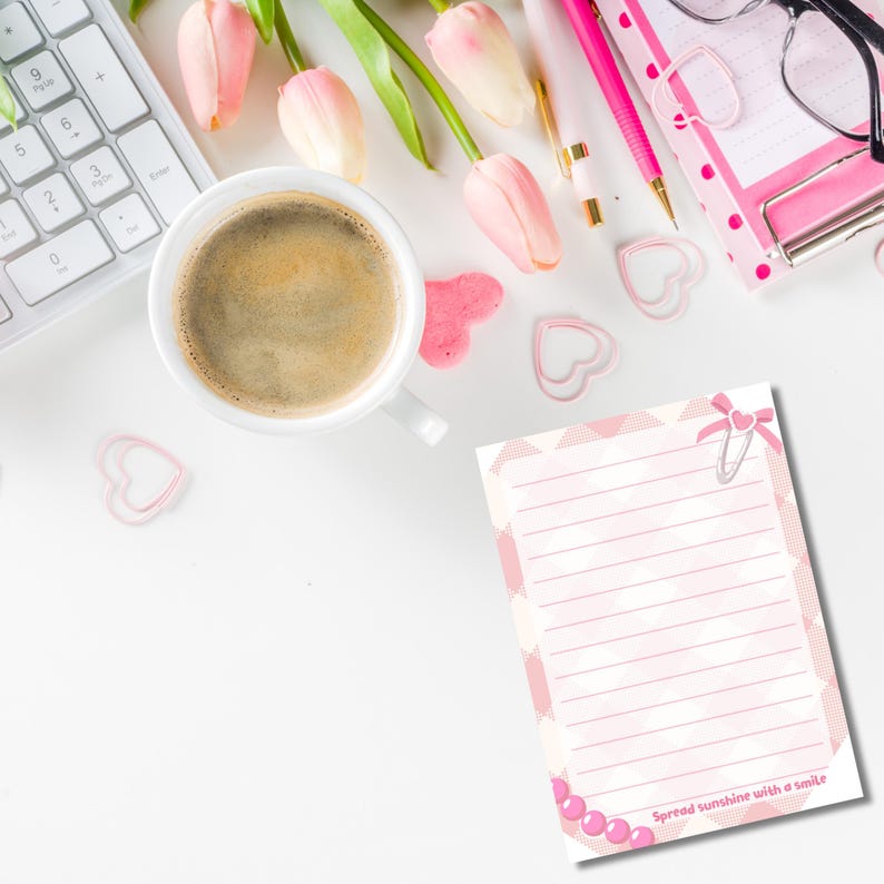 May include: A white desk scene with a cup of coffee, pink tulips, and stationery. A notepad with the text "Spread sunshine with a smile" is visible, along with heart-shaped paper clips and a keyboard. The scene is bright and airy.