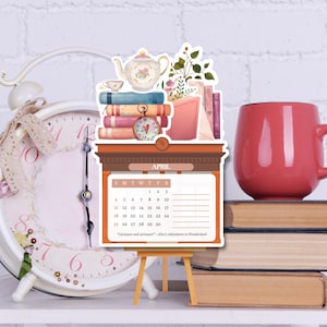 May include: A die-cut calendar for April featuring a stack of books, a teapot, and a pocket watch. The calendar displays the month of April with the text "Curiouser and curiouser!" from Alice's Adventures in Wonderland, supported by a small wooden easel.