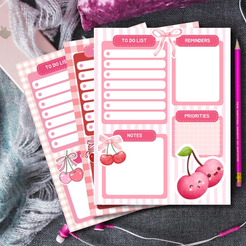 May include: Pink and white to-do list notepads with cherry illustrations. The notepads feature sections for to-do lists, reminders, notes, and priorities. A pink pencil and earbuds are also visible.