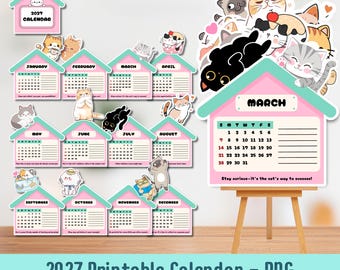 May include: A 2027 printable calendar set featuring twelve house-shaped monthly pages with pastel pink and teal accents. Each page displays a grid for dates and cartoon cat illustrations. A larger March page is displayed on a wooden easel.