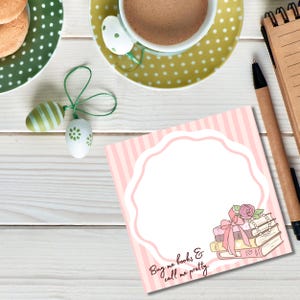 K&ouml;nnte beinhalten: Draufsicht auf einen rosa-wei&szlig; gestreiften Notizblock mit dekorativem Rand und dem Text "Buy me books & call me pretty." Ein Stapel B&uuml;cher mit Schleife und Perlen befindet sich in der Ecke. Eine Tasse Kaffee, Kekse und dekorative Eier sind ebenfalls vorhanden.